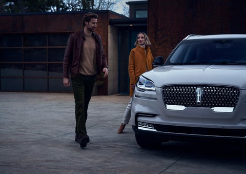A man and a woman approaching a 2024 Lincoln Aviator® SUV, which illuminates certain lights when they are close | Beach Lincoln in Myrtle Beach SC