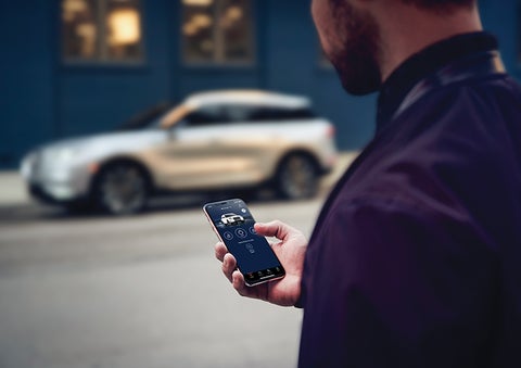 A person is shown interacting with a smartphone to connect to a Lincoln vehicle across the street. | Beach Lincoln in Myrtle Beach SC