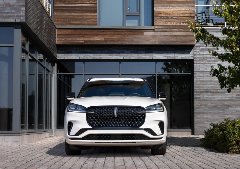 A white 2025 Lincoln Aviator® SUV is shown parked outside a modern building with gray brick and wood accents. | Beach Lincoln in Myrtle Beach SC