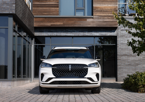 A white 2025 Lincoln Aviator® SUV is shown parked outside a modern building with gray brick and wood accents. | Beach Lincoln in Myrtle Beach SC