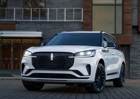 A white 2025 Lincoln Aviator® SUV is shown parked outside a modern building with gray brick and wood accents. | Beach Lincoln in Myrtle Beach SC